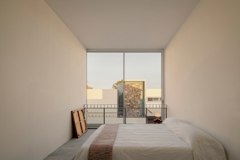 Bedroom with low platform bed facing a glazed door opening onto a courtyard at dusk