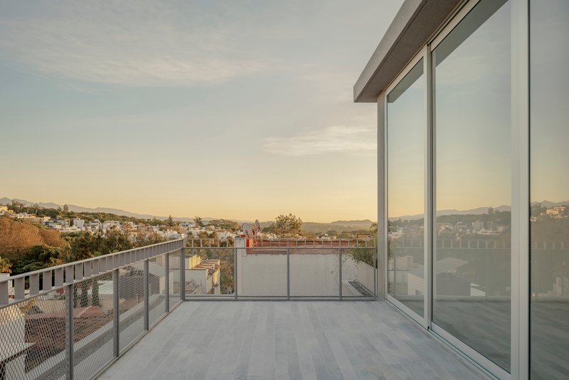 Rooftop terrace with metal mesh railing overlooking a hilly residential neighborhood at sunset