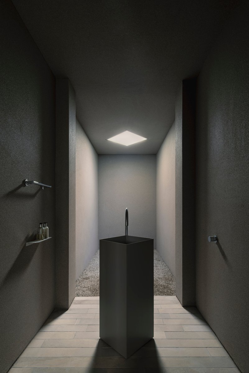 Narrow corridor with dark textured walls and a single skylight illuminating a black pedestal sink