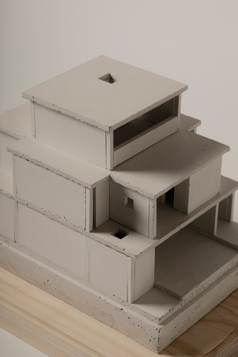 Close-up of a concrete study model with stacked volumes and open voids on a plywood base