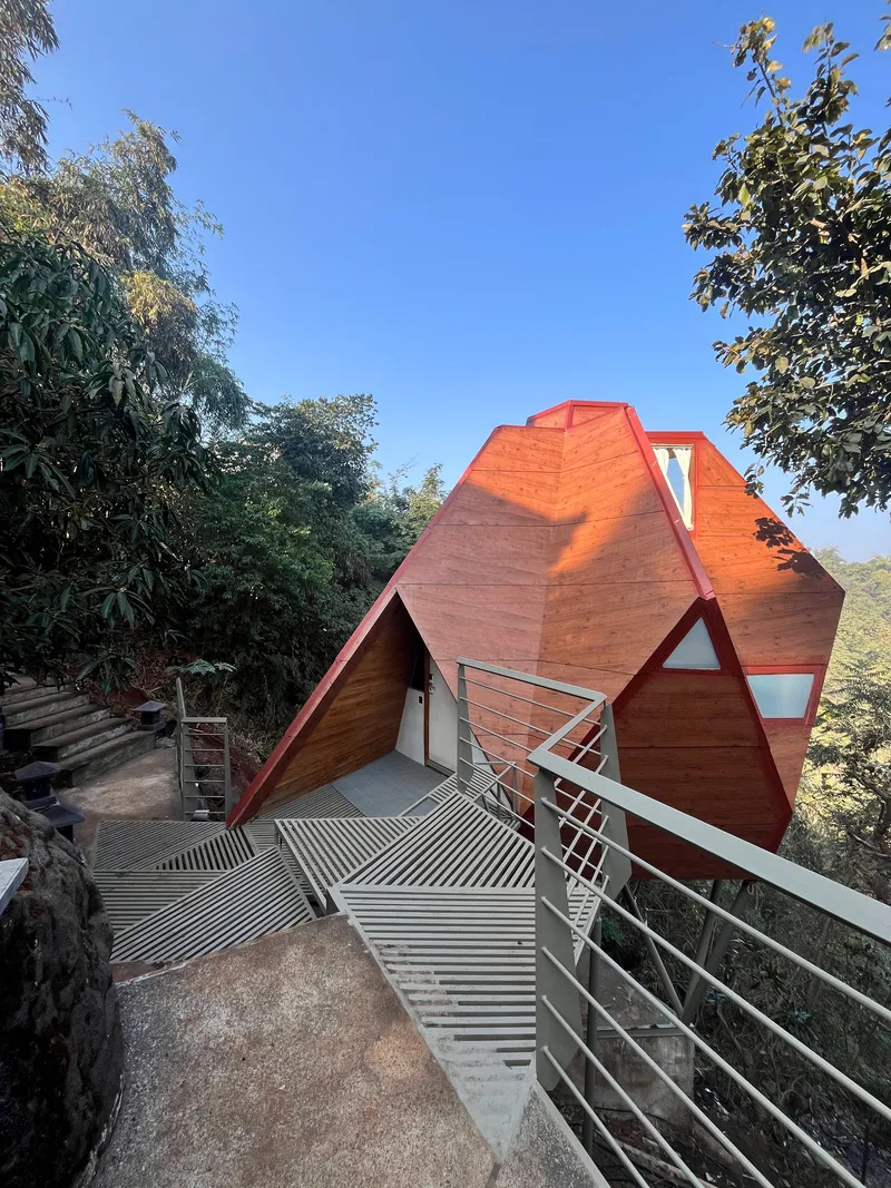 Exterior terrace with grated metal floor and railing facing a faceted terracotta pyramid beneath blue sky