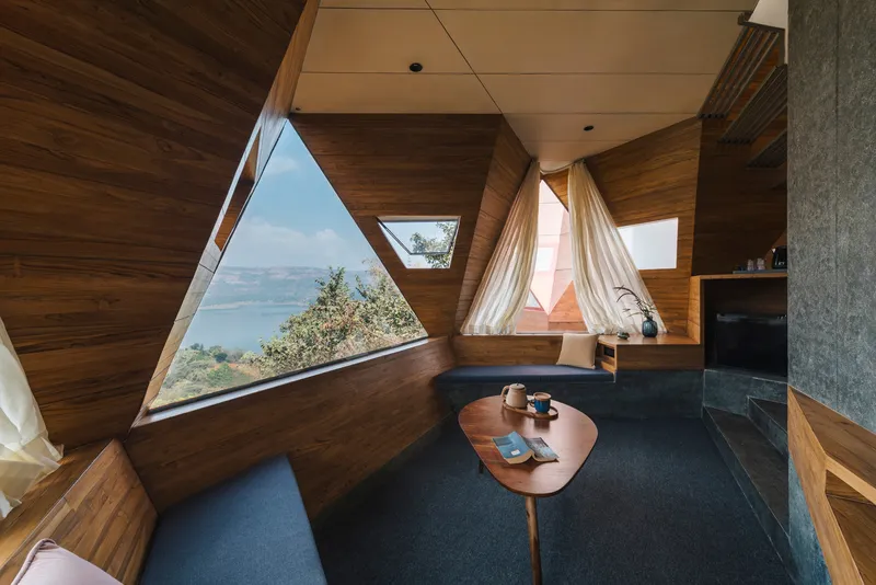 Sitting area with timber-clad angular walls and triangular window framing a distant lake view