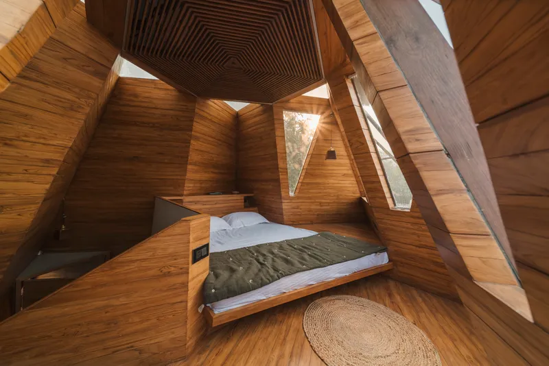 Timber-lined bedroom with chevron-patterned ceiling and angled triangular window casting afternoon light