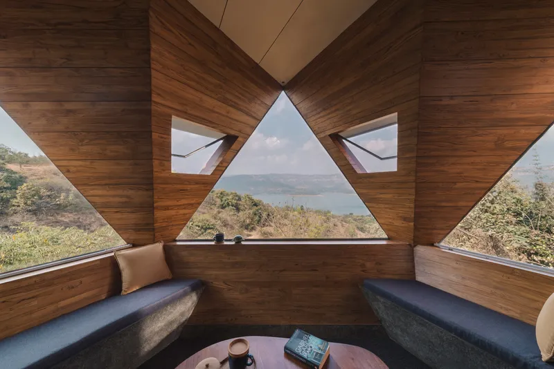Built-in seating nook with triangular window overlooking forested hills and distant water under daytime sky