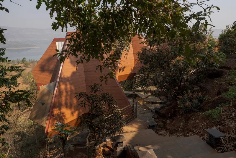 Pyramidal timber structure rising from hillside site with lake visible in distant valley beyond