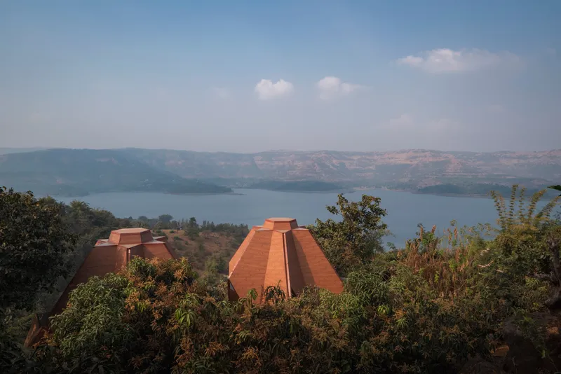 Distant view of red terracotta pyramidal roofs emerging from trees overlooking a wide reservoir and hills