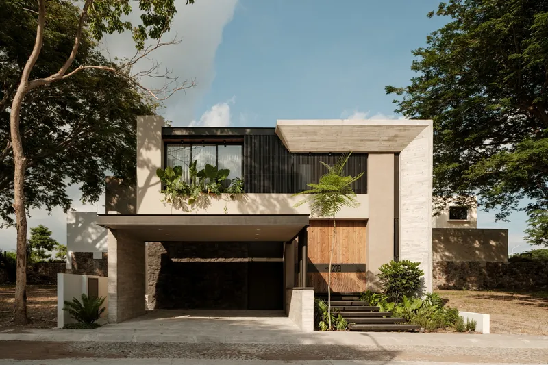 Street facade with white stucco, dark vertical slats, and timber cladding framed by mature trees