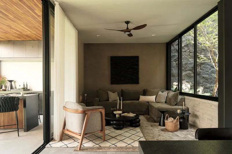 Living room opening to kitchen through black-framed glazing with sheer curtains and patterned floor tiles