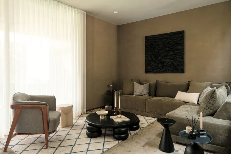 Living room with tan plaster walls, sheer curtains filtering daylight, and a sectional sofa facing black tables