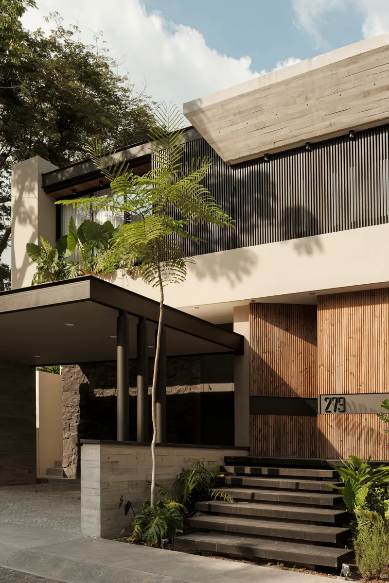 Street facade with vertical wood slat cladding, board-formed concrete canopy, and palm tree shadows