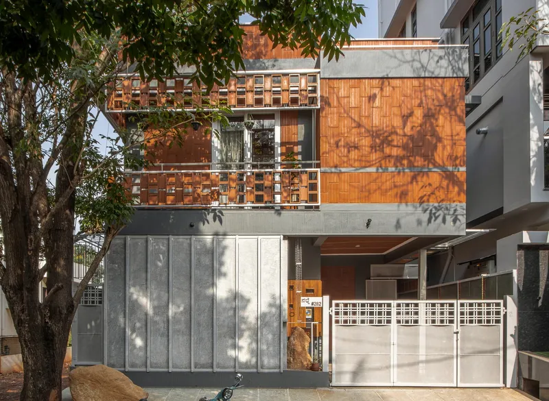 Street facade with orange terracotta tile screens above grey metal panels and dappled tree shadows