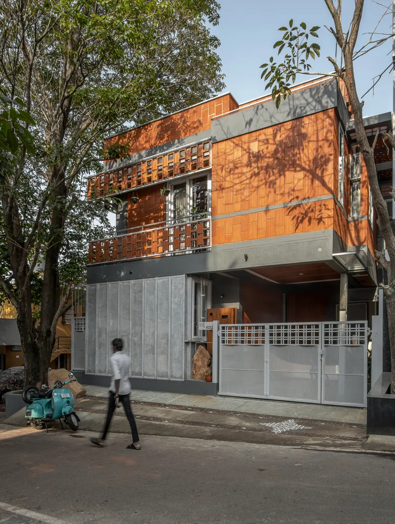 Street view showing layered facade with terracotta screens and pedestrian passing on the sidewalk