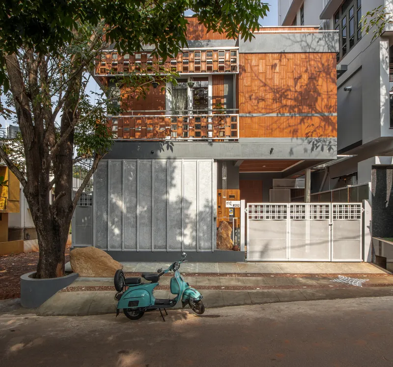 Street facade with concrete panels below and terracotta brickwork above, shaded by a large street tree