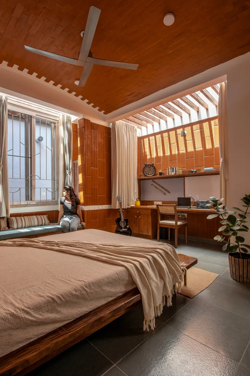 Bedroom with slatted timber ceiling, clerestory window, and person seated by the window with a guitar