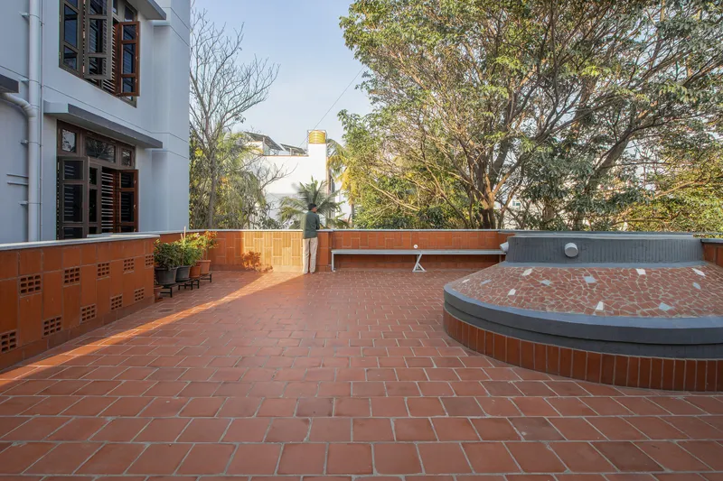 Rooftop terrace with red clay tile paving and circular planters beneath mature trees