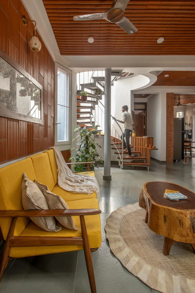 Double-height living space with spiral stair and timber slatted ceiling as a person ascends