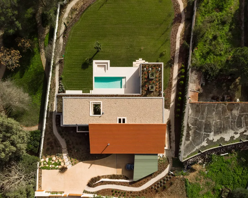 Aerial view of the residence showing white and timber volumes with pool and green roof terrace