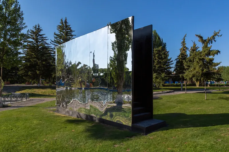 Polished metal panel with black reverse side standing in park framed by evergreen trees