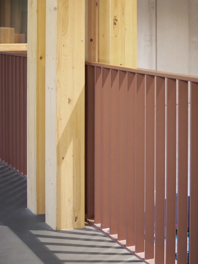Corner detail showing timber column beside terracotta-colored vertical slat panel casting diagonal shadows