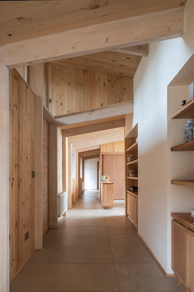 Corridor with exposed timber beams and shelving recessed into white plaster walls