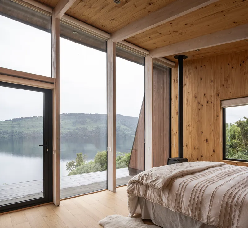 Bedroom with full-height glazing and black flue pipe framing views across the water
