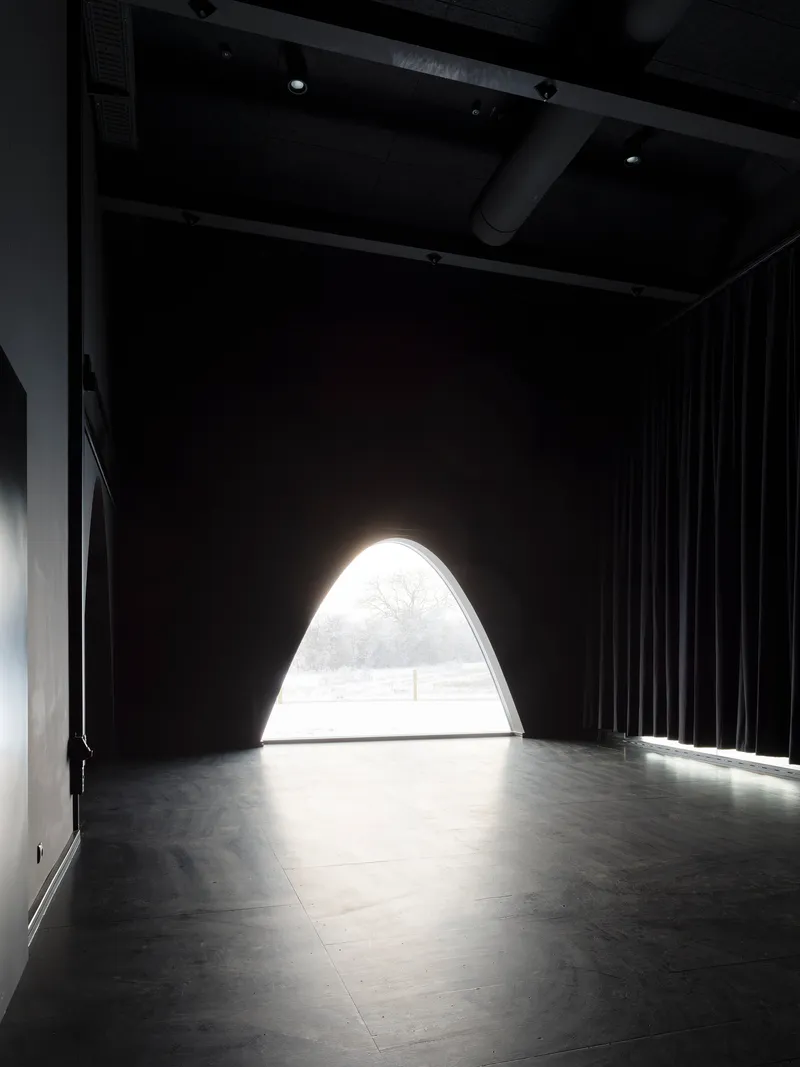 Arched opening flooding light into a dark performance space with black curtains and exposed ceiling