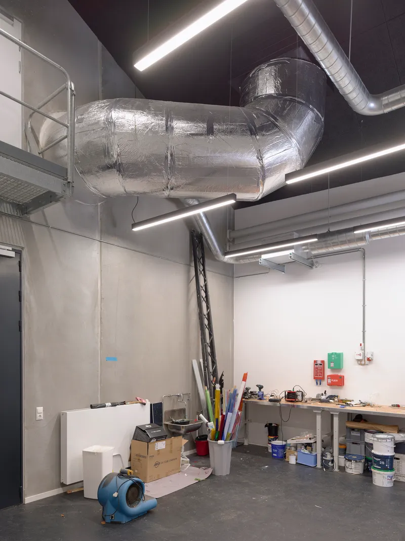 Exposed mechanical room with insulated spiral ductwork suspended above concrete walls and a work table