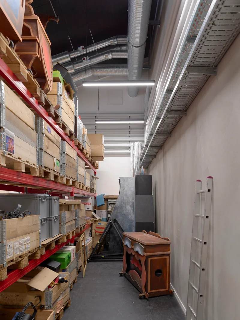 Storage corridor with red metal shelving units stacked with wooden crates below exposed ceiling ducts