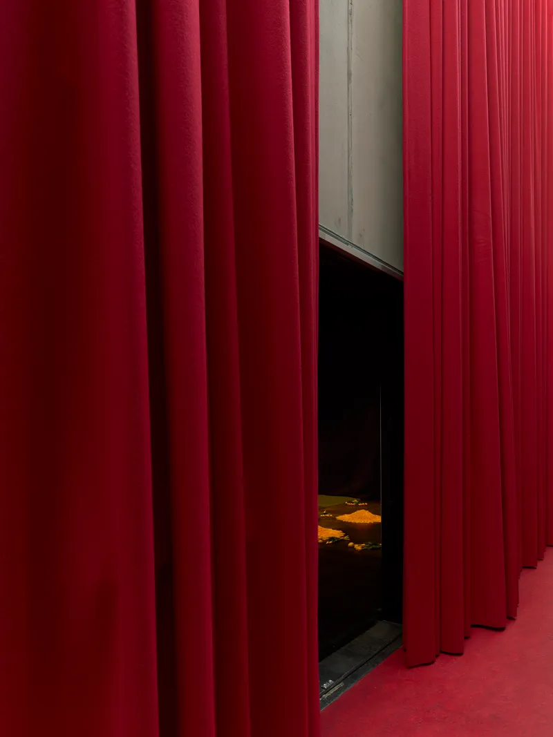 Deep red fabric curtains parted to reveal a dark theater space with painted floor visible beyond