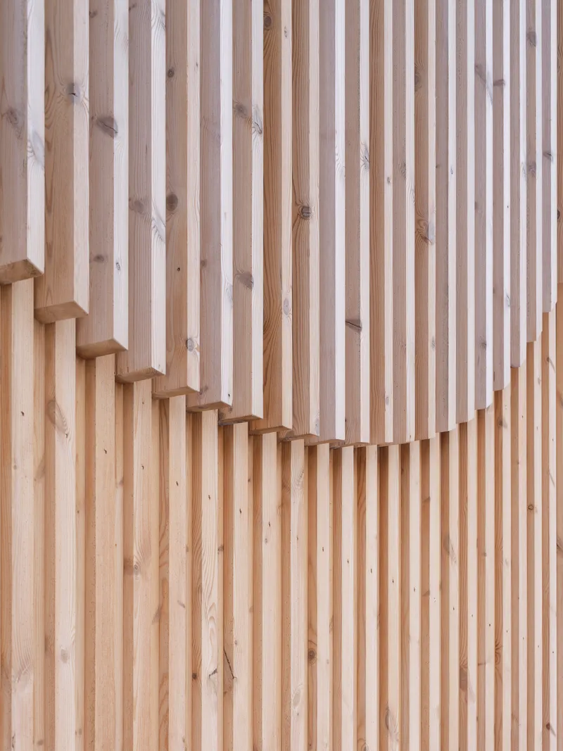 Vertical timber slat wall with a cantilevered wooden staircase rising diagonally across the surface