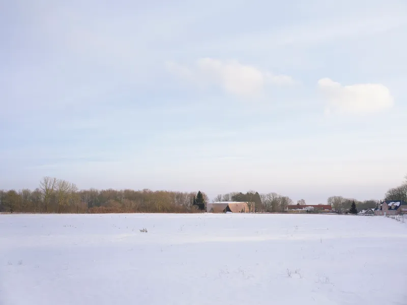 Distant view of the structure across an expansive snowfield with a tree line on the horizon