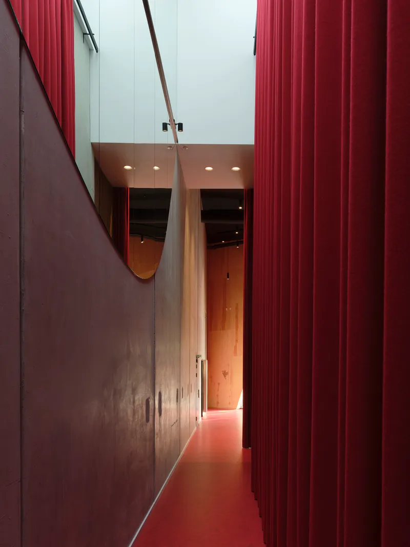 Narrow corridor with red floor and corrugated wall panels leading to a mirrored archway above
