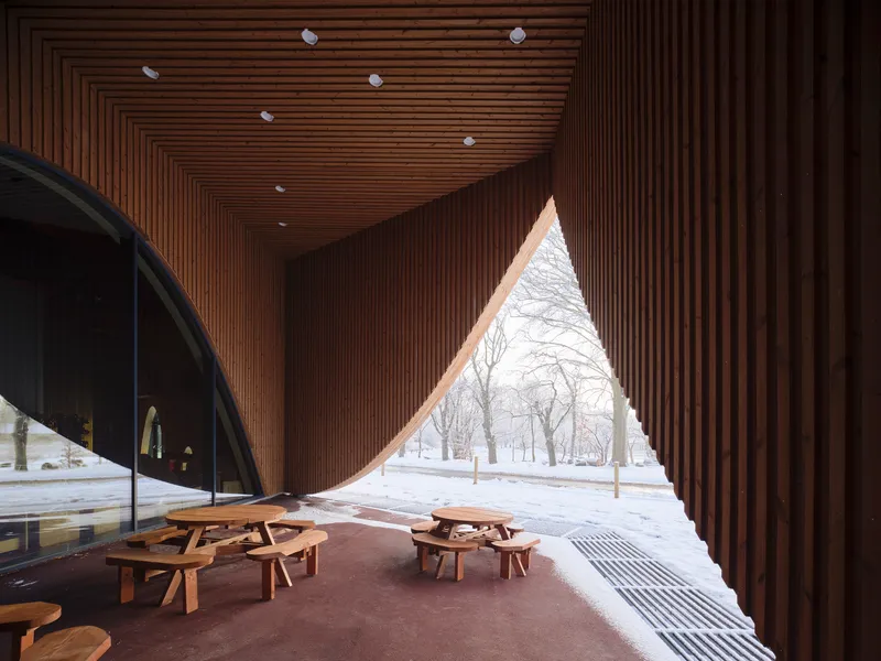 Slatted timber ceiling over a covered porch with triangular opening framing snowy park benches outside
