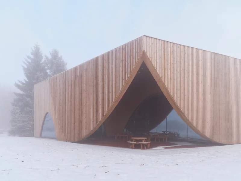 Sheltered outdoor space beneath a peaked timber canopy with picnic tables visible through fog