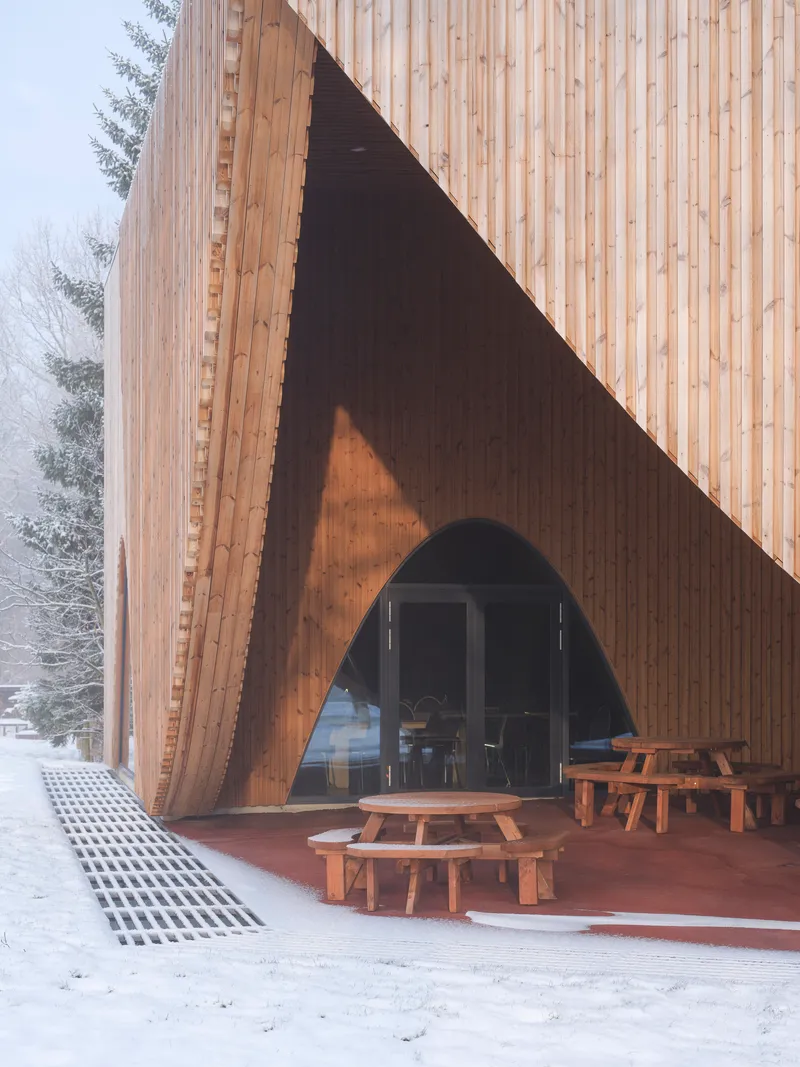 Triangular entrance opening framed by timber cladding with picnic benches on the covered terrace in snow