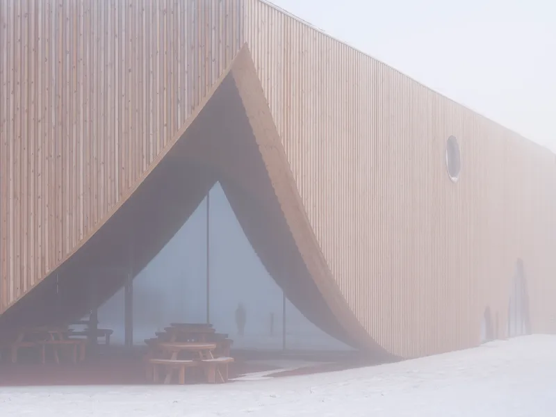 Timber-clad facade with triangular glazed entrance in heavy fog and fresh snow