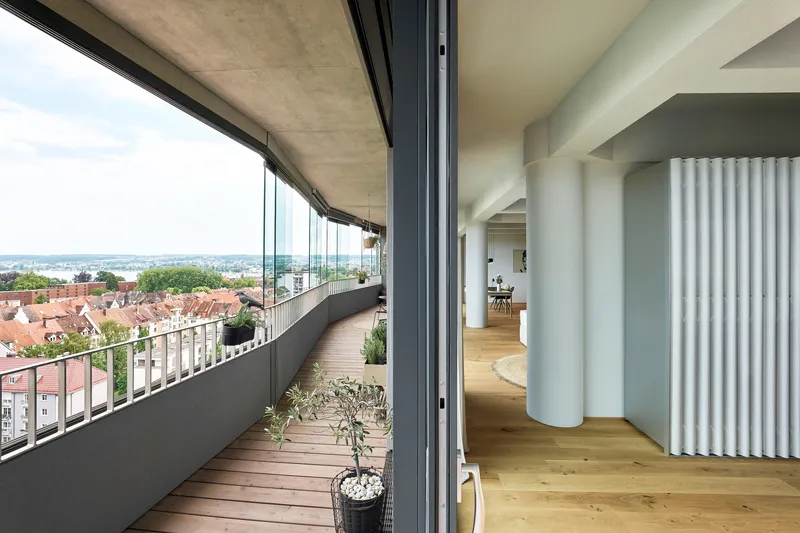 Wooden deck balcony with potted olive tree opening through sliding glass to fluted interior columns