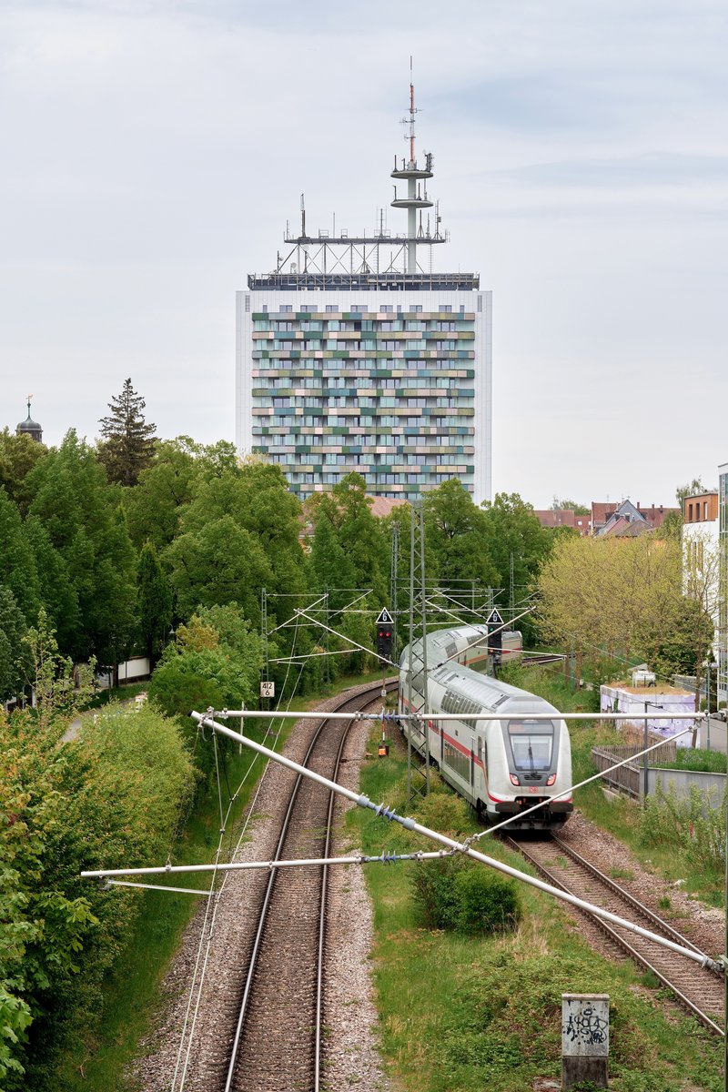 Residential tower with telecommunications antenna above railway tracks and passing commuter train in spring