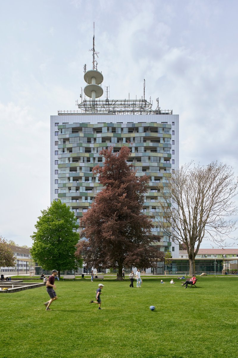 White tower with multicoloured balconies and rooftop antenna array behind a park lawn with children playing