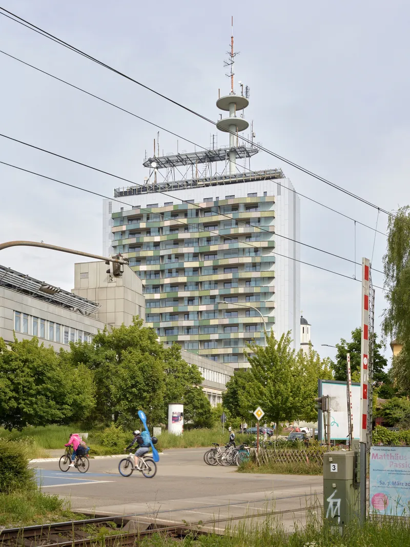 Residential tower with patterned balcony facade viewed from the street with overhead tram cables and cyclists passing