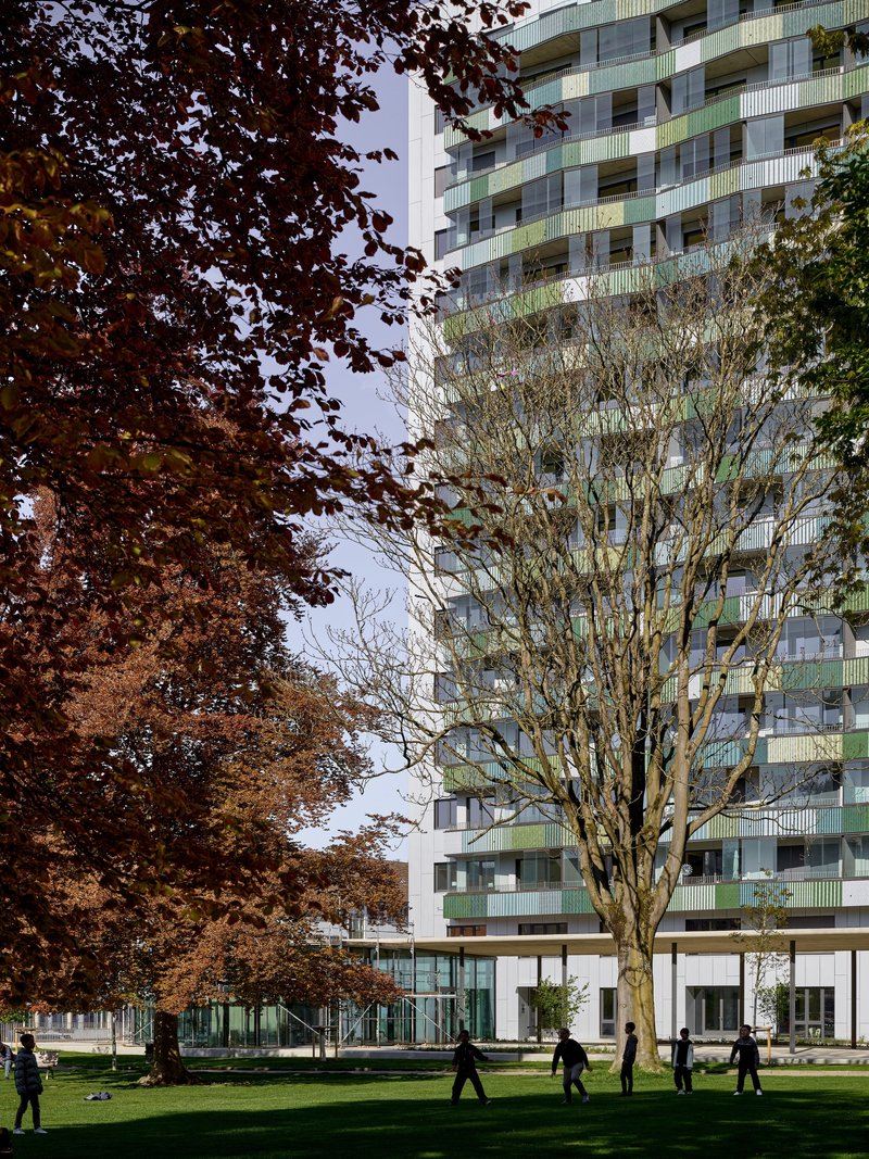 Facade with glass balconies and green railings partially obscured by autumn trees in the park below