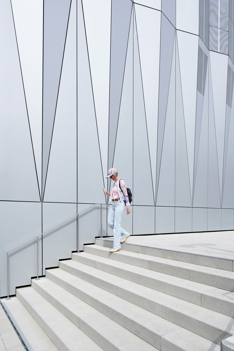 Exterior staircase with metal handrail against a white panel facade with angular black joint lines