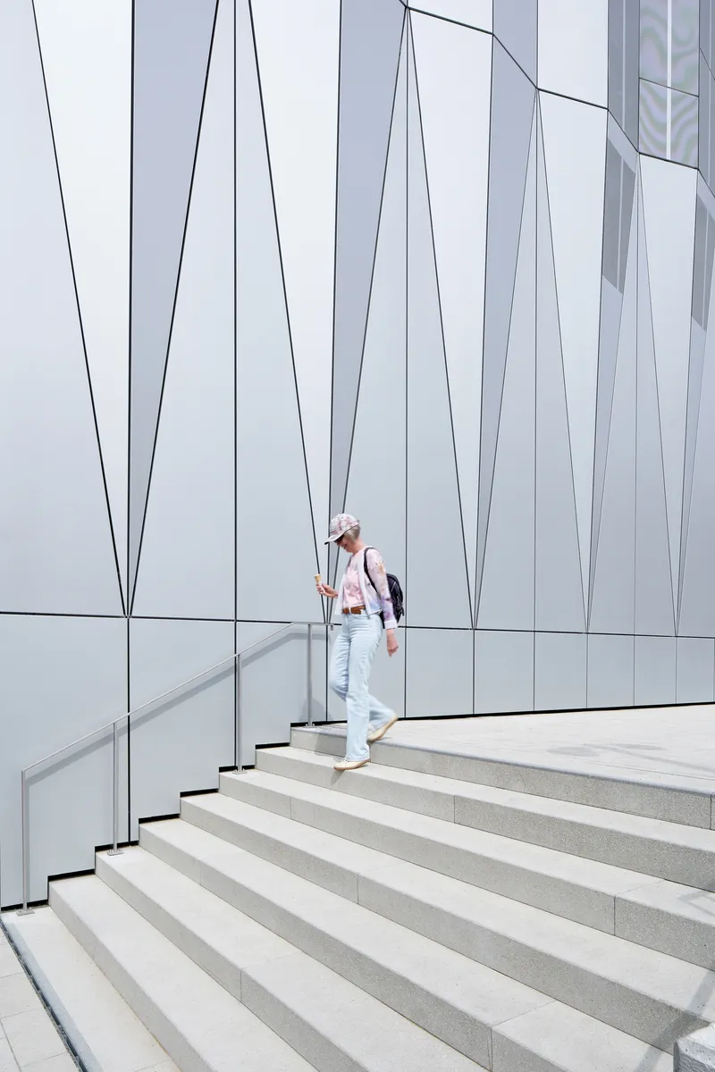 Exterior staircase with metal handrail against a white panel facade with angular black joint lines