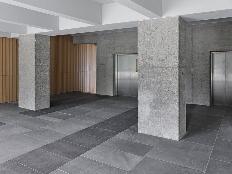 Entrance lobby with textured concrete columns, polished grey tile flooring and stainless steel elevator doors