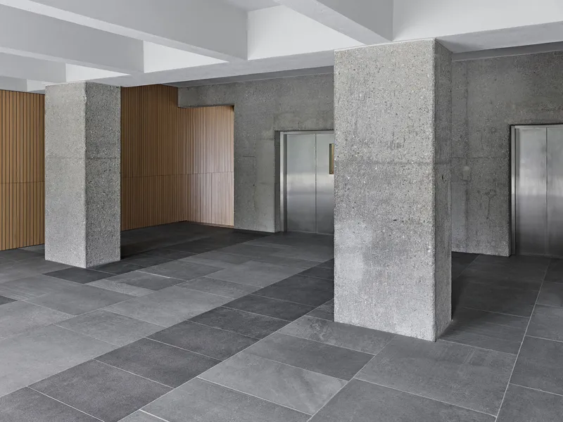 Entrance lobby with textured concrete columns, polished grey tile flooring and stainless steel elevator doors