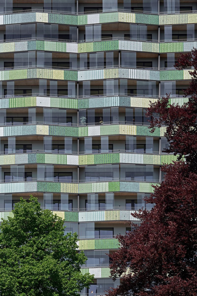 Facade detail showing stacked balconies with green and yellow railings flanked by red and green trees