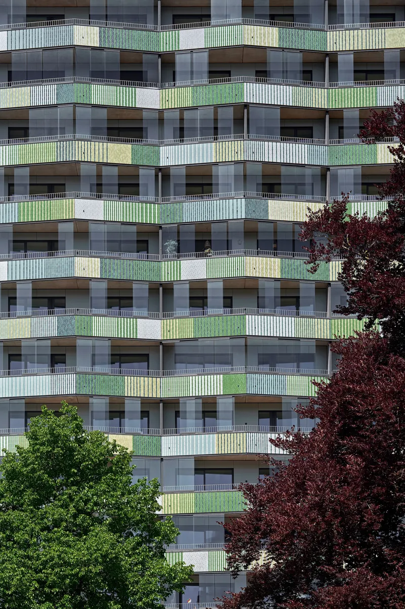 Facade detail showing stacked balconies with green and yellow railings flanked by red and green trees