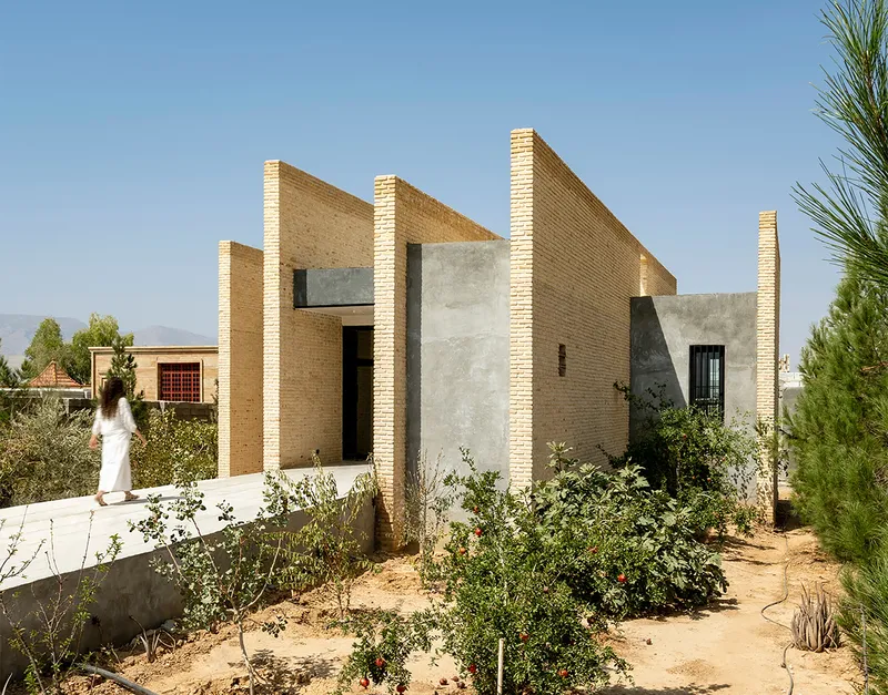 Facade composition of buff brick walls and concrete panels with triangular rooflines amid native plantings