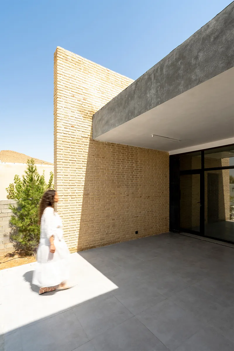Entry courtyard corner showing tall brick screen wall meeting concrete overhang as person passes through