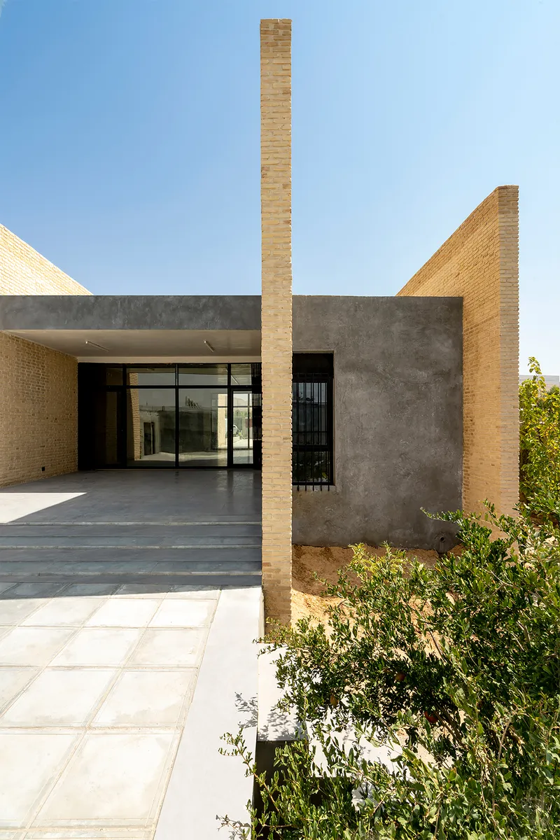 Exterior threshold with slender brick column dividing entrance porch from planted garden bed at edge